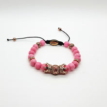 Load image into Gallery viewer, A pink beaded bracelet with a central metallic dragon charm, gold spacer beads, and a black adjustable cord with a branded tag.
